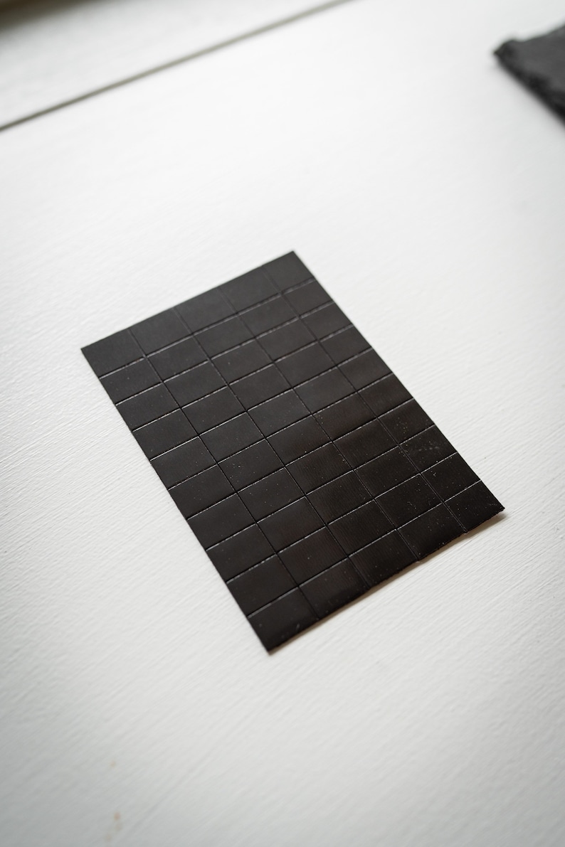 Op de afbeelding: Een zwarte magnetische plaat met een rasterpatroon. De plaat is gemaakt van kleine vierkanten.