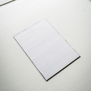 Op de afbeelding: Een witte rechthoekige kaart met een licht ruwe textuur. De kaart ligt plat op een wit oppervlak.