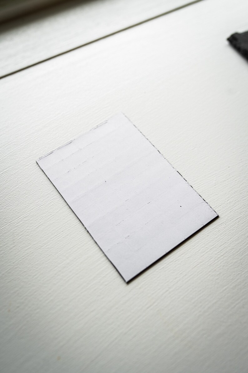 Op de afbeelding: Een witte rechthoekige kaart met een licht ruwe textuur. De kaart ligt plat op een wit oppervlak.