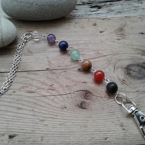 May include: A silver chain keyring with seven colourful beads, including clear, purple, blue, green, brown, red and black beads. The keyring has a silver clip.