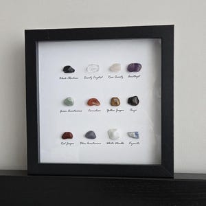 May include: A framed display of 12 different types of stones, including black obsidian, rose quartz, amethyst, green aventurine, carnelian, yellow jasper, onyx, red jasper, blue aventurine, white marble, and kyanite.