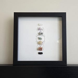 May include: A black framed picture with a white background and a geometric design with seven crystals in different colors and shapes.