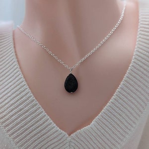 May include: A silver chain necklace with a black lava rock pendant in the shape of a teardrop.