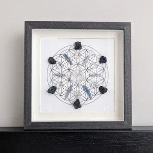 Peut inclure: Une impression encadrée d'une grille de cristal avec un motif de fleur de vie. La grille présente des cristaux de quartz clair, des cristaux de kyanite bleue et des cristaux d'obsidienne noire.