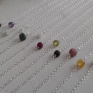 May include: A collection of silver chains with various colored gemstone beads. The beads are arranged in a row, with each chain having a different color bead.