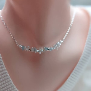 May include: A delicate silver necklace featuring small, light blue and clear crystal beads. The beads are strung along a fine silver chain, creating a subtle and elegant accessory. The necklace is designed to sit gracefully on the neckline.