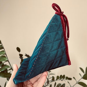May include: A teal blue velvet pillow with a quilted pattern and a red velvet trim. The pillow has a red velvet tie at the top.