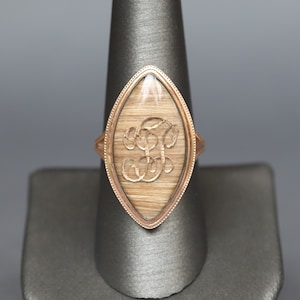 May include: A gold ring with a clear oval-shaped stone. The stone contains a monogram of the letters "F" and "B" in a cursive script.