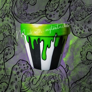 Pode incluir: Um vaso de cerâmica listrado de verde e branco com tinta verde pingando. O vaso é decorado com o texto "Made with my tentacles". O vaso é cercado por uma ilustração em preto e branco de tentáculos.