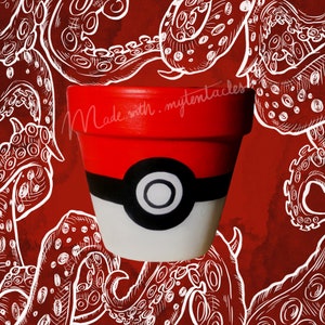 Può includere: Un vaso di ceramica rosso, bianco e nero con un design a Poké Ball. Il vaso è circondato da un contorno bianco di tentacoli su uno sfondo rosso. Il testo "Made with my tentacles" è scritto sul vaso.
