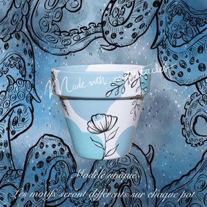 Pode incluir: Um vaso de flores de cerâmica pintado à mão com um design azul claro e branco. O vaso apresenta uma ilustração floral preta e o texto "Made with" e "Modele unique". O fundo tem um design de polvo azul.