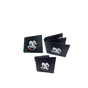 Könnte beinhalten: Drei schwarze Ledergeldbörsen mit einem gestickten Comic-Katzenkopf auf der Vorderseite. Die Katze hat ein weißes Gesicht mit schwarzen Augen und einem roten Mund.