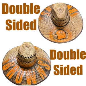 May include: Double-sided straw hat with orange and brown paint. The hat has a woven design and the words "Double Sided" are written on the hat.