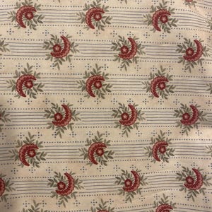 May include: Cream-colored fabric with a repeating pattern of red floral designs and green leaves. The design is interspersed with thin, horizontal blue stripes and dotted lines, creating a vintage aesthetic.
