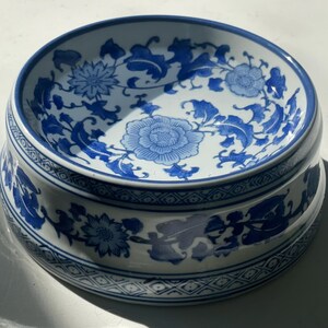以下が含まれることがあります： 青と白の花柄が施された白い陶器のボウル。ボウルは縁が高く、波打った縁をしています。