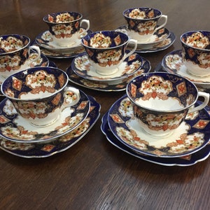 May include: A set of six teacups and saucers featuring a blue and gold floral pattern. The cups and saucers are crafted from fine china and have a delicate design.