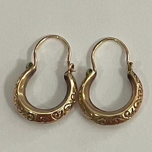 Peut inclure: Une paire de créoles dorées présentant une base incurvée et épaisse avec un motif complexe de volutes en relief sur toute la surface. Chaque boucle d'oreille comprend un mécanisme de fermeture à fil fin simple sur le dessus.
