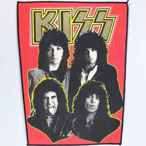 May include: A rectangular patch featuring the band KISS. The band's name is in gold glitter lettering above four band members' portraits. The background is red with a black border.