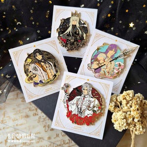 May include: A collection of enamel pins featuring detailed illustrations of anime-style characters. Each pin is a different design, with vibrant colors and intricate details. The pins are displayed on decorative cards with gold accents.