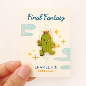 Könnte beinhalten: Goldene Emaille-Anstecknadel mit einem grünen Kaktus-Charakter aus der Final Fantasy-Videospielserie. Die Anstecknadel hat einen gelben Umriss und eine rote Krone oben. Der Text "Final Fantasy" und "Enamel Pin" ist auf der Karte gedruckt.