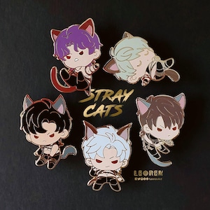 Può includere: Cinque spille in smalto dorate raffiguranti personaggi dei cartoni animati con orecchie da gatto. I personaggi indossano abiti diversi e hanno colori di capelli diversi. Le spille sono disposte in cerchio attorno alle parole "Stray Cats".