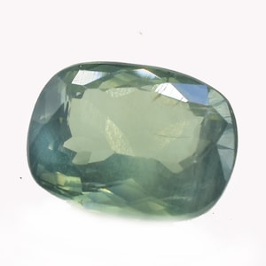 Puede incluir: Una gema facetada, de forma ovalada, con una mezcla de tonos verdes y azules. La gema se encuentra sobre un fondo blanco, mostrando su claridad y el juego de la luz en sus múltiples facetas. La gema parece ser un zafiro.