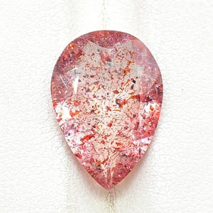 May include: A clear, pear-shaped gemstone with red and orange inclusions. The faceted gem sparkles, reflecting light. The stone is set against a white background. The gem's shape is reminiscent of a teardrop.