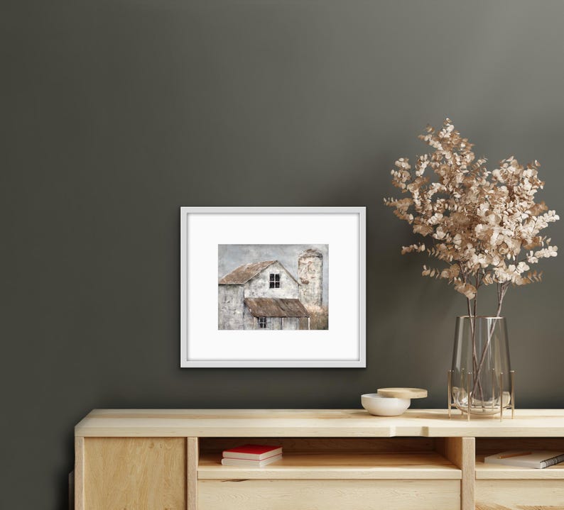 May include: A framed print of a weathered white farmhouse with a silo, set against a cloudy sky. The farmhouse has a single window and a brown roof.