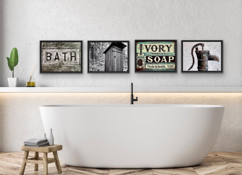 May include: Four framed vintage-style prints above a white bathtub. The prints feature the word "BATH", a black and white photo of an outhouse, an "IVORY SOAP" advertisement, and a water pump. The bathroom has a wooden stool and a green plant.