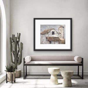 May include: A framed painting of a weathered farmhouse with a silo, painted in muted tones of brown, gray, and white. The painting is displayed on a wall above a light pink bench with black metal legs.
