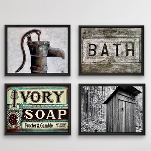 May include: Four framed wall art pieces. One features a rustic water pump, another reads "BATH" in bold letters. A third displays an "IVORY SOAP" sign, and the last is a black and white photo of a wooden outhouse.