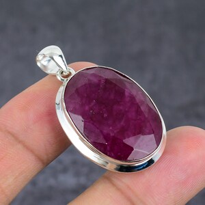 Peut inclure: Un pendentif de forme ovale avec une grande pierre précieuse facettée magenta foncé sertie dans une monture en argent poli. Le pendentif comprend une bélière en argent sur le dessus pour l'attacher à une chaîne, avec une finition métallique lisse.