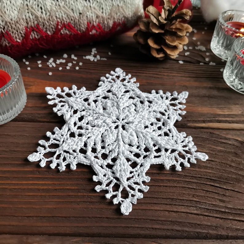 May include: White crocheted snowflake on a brown wooden surface.