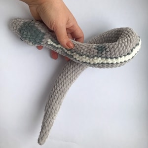 May include: A gray and white crocheted snake toy. The snake is curled up in a circle.
