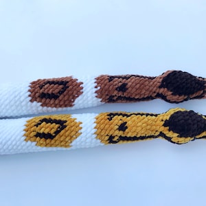 May include: Two crocheted snakes with white, brown, and yellow patterns. The snakes are made with a fuzzy yarn and have black eyes.