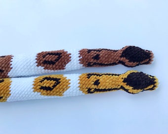 May include: Two crocheted snakes with white, brown, and yellow patterns. The snakes are made with a fuzzy yarn and have black eyes.