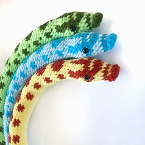 Peut inclure: Trois serpents en crochet dans un arc-en-ciel de couleurs. Le serpent du haut est vert, le serpent du milieu est bleu et le serpent du bas est rouge et jaune.