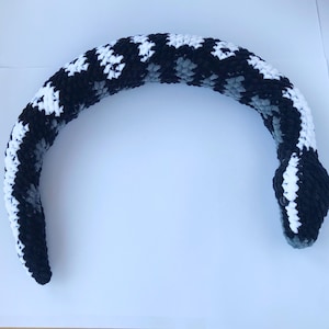 May include: A black and white crocheted snake toy. The snake is curled into a circle shape.