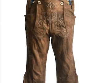 May include: Brown leather lederhosen with decorative stitching and button closures. The knee-length pants feature pockets and side ties. The traditional Bavarian style is displayed against a white background.