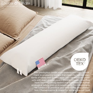 May include: A white body pillow with a "Made in USA" label and the OEKO-TEX&reg; logo. The pillow is on a bed with a brown and gray patterned blanket. The text "Looms & Linens An American Dream" is at the top of the image.