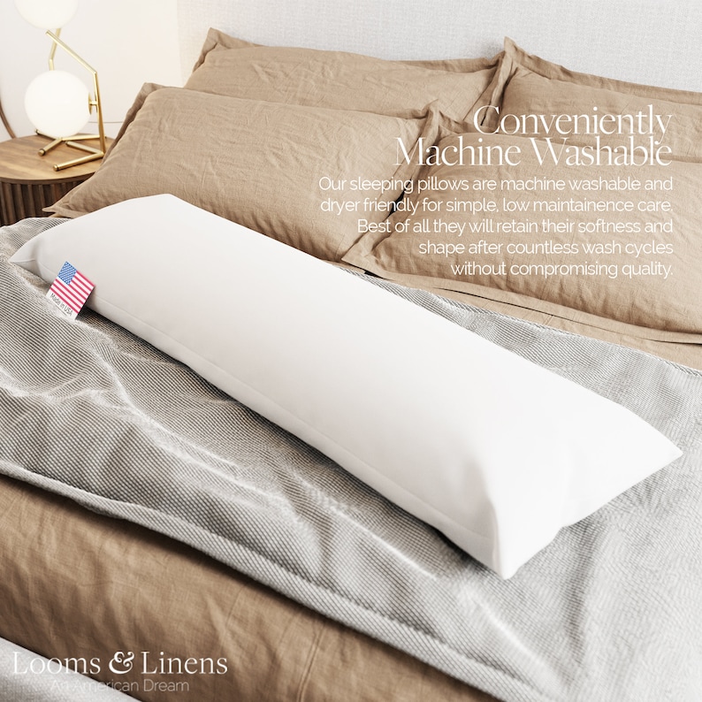 May include: A white body pillow on a bed with a tan and gray patterned blanket. The pillow is labeled "Conveniently Machine Washable" and "Our sleeping pillows are machine washable and dryer friendly for simple, low maintenance care. Best of all they will retain their softness and shape after countless wash cycles without compromising quality."