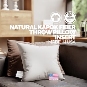 May include: A white square throw pillow with a brown pillow behind it, resting on a dark gray couch. The text on the pillow reads "NATURAL KAPOK FIBER THROW PILLOW INSERT MADE IN USA". The image also includes a "Vegan 100%" logo.