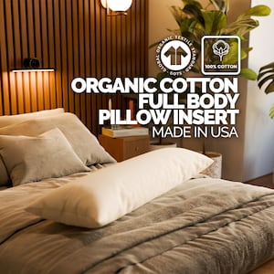 May include: A full body pillow insert made of organic cotton, resting on a bed with other pillows and a blanket. The text on the image reads "ORGANIC COTTON FULL BODY PILLOW INSERT MADE IN USA". The pillow is a light cream color.