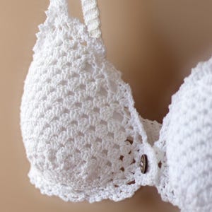 Può includere: Top di bikini bianco all'uncinetto con chiusura a bottone. La parte superiore è realizzata in un tessuto delicato e traforato.