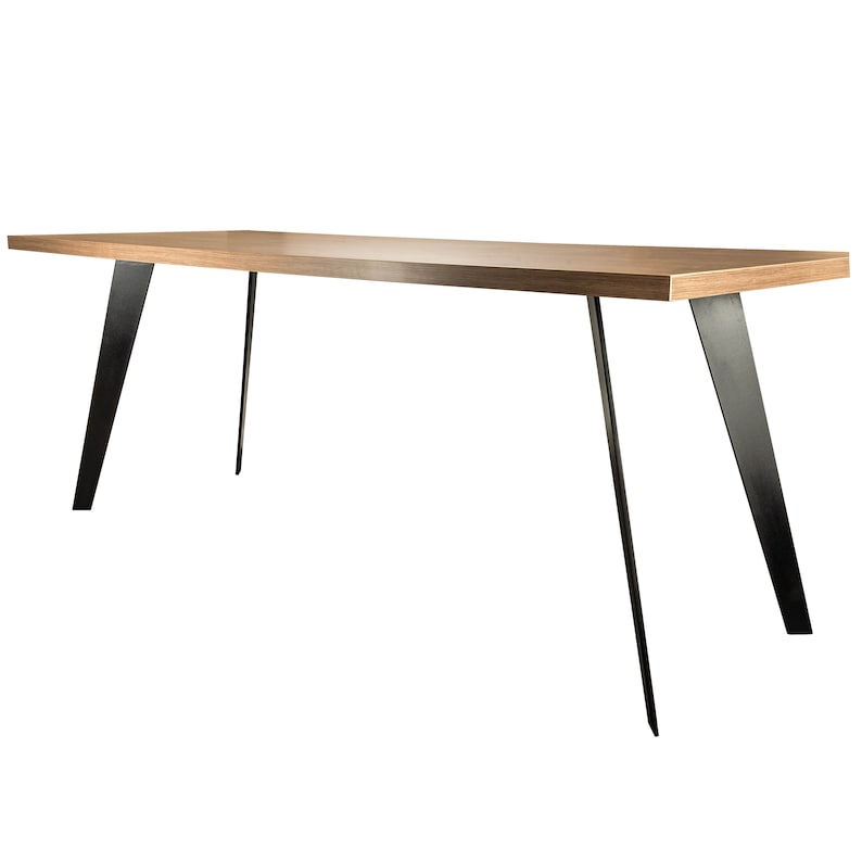 Op de afbeelding: Een lange, rechthoekige houten tafel met een lichtbruine afwerking en zwarte metalen poten. De poten zijn schuin en steken uit de tafelblad.