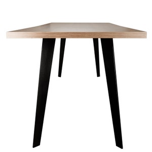 Op de afbeelding: Een rechthoekige houten tafel met een lichtbruin blad en zwarte metalen poten. De poten zijn schuin en steken uit onder het tafelblad.