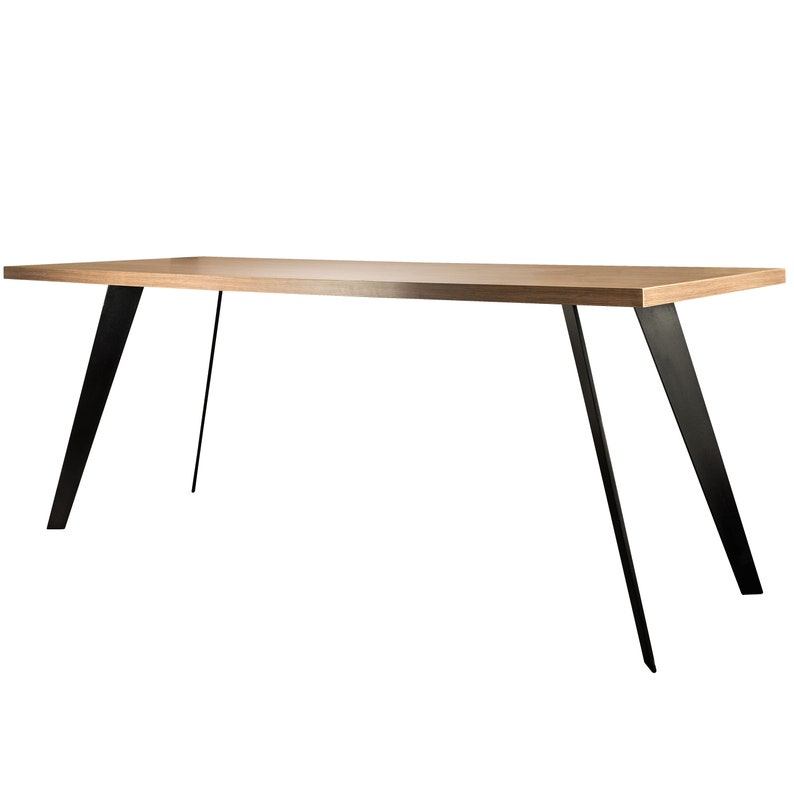 Op de afbeelding: Een lange, rechthoekige houten tafel met een lichtbruine afwerking en zwarte metalen poten. De poten zijn schuin en cre&euml;ren een modern, minimalistisch ontwerp.