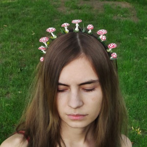May include: A woman with long brown hair wearing a headband with red and white mushroom decorations.