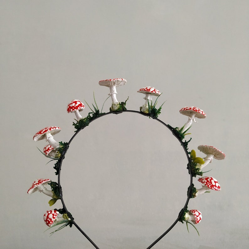 May include: A black headband with red and white mushroom decorations. The mushrooms are arranged in a circle around the headband.