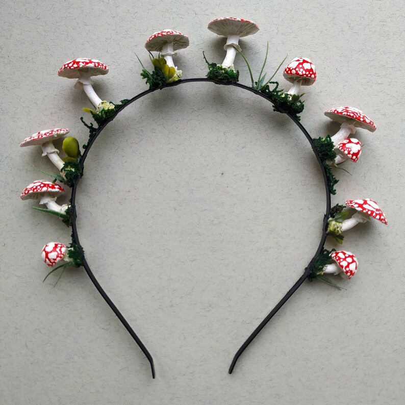 May include: A black headband with red and white mushroom decorations. The mushrooms are attached to the headband with green leaves.